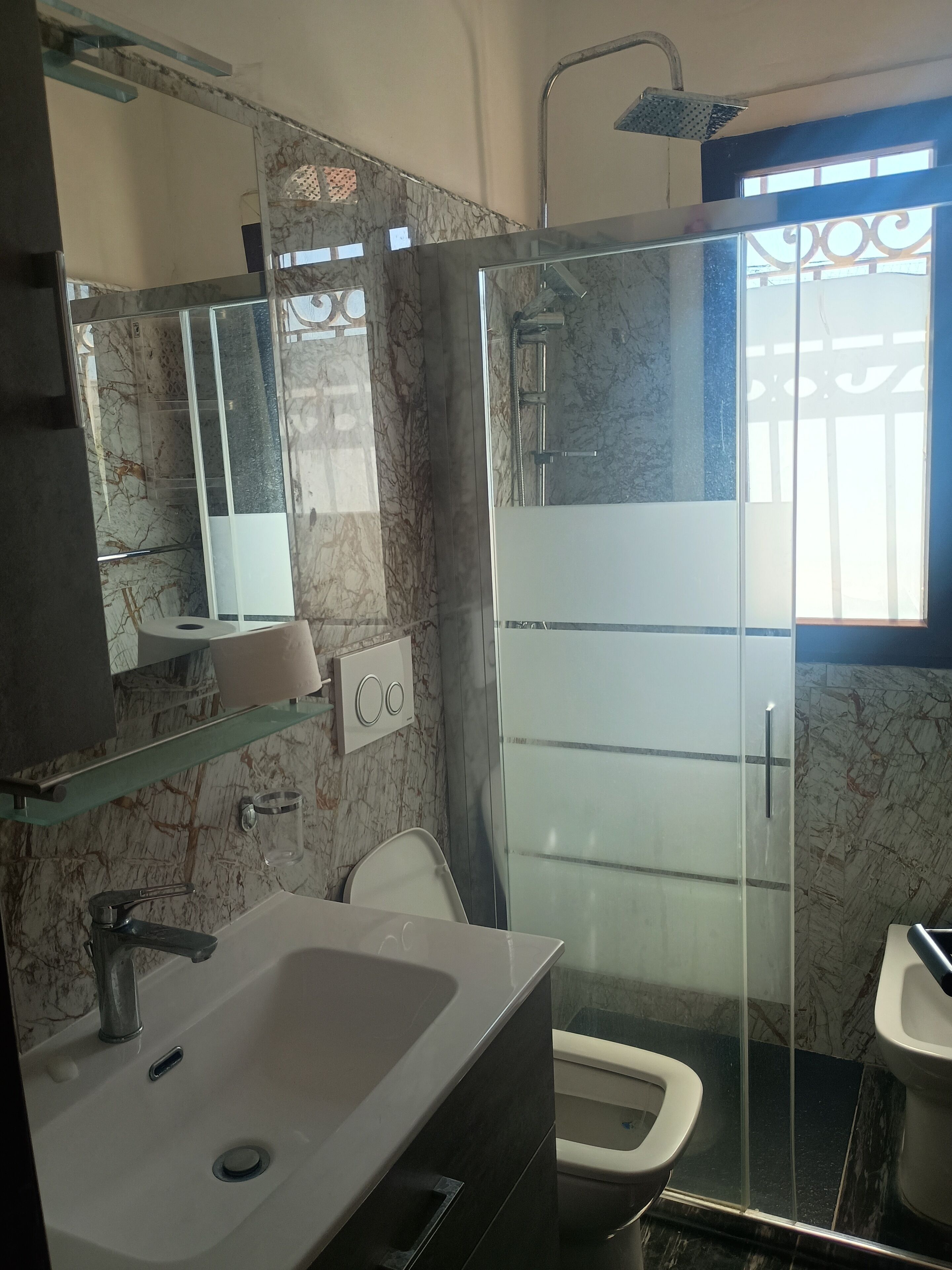 Une salle de bain avec un lavabo, un miroir, une douche, des toilettes et des murs en marbre.