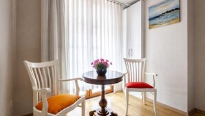 A room with a round wooden table, two white chairs with cushions, a window with sheer curtains, and a painting on the wall. - My Way Teras Hotel (Adalar)