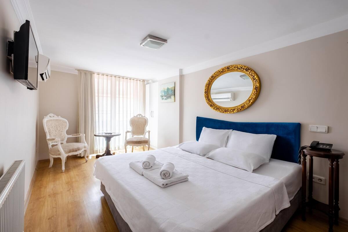 A hotel room with a bed, a chair, a small table, a mirror, and a television.