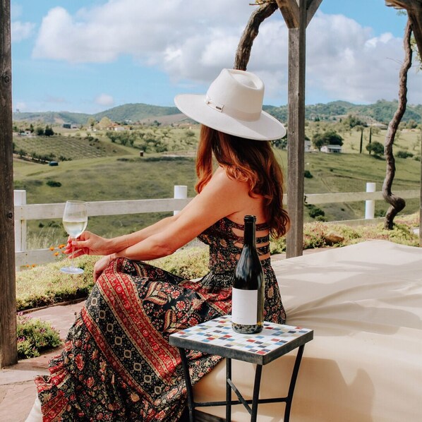 A person seated at a table with a bottle of wine and a glass, overlooking a scenic landscape. - FarmStay HillTop wine country views 4BR/4BA (Paso Robles)
