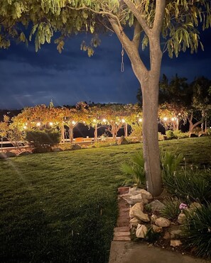 A well-maintained garden with a paved walkway, a pergola with string lights, and a large tree. - FarmStay HillTop wine country views 4BR/4BA (Paso Robles)