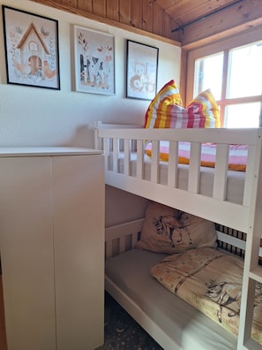 A bunk bed with a pillow featuring a horse design, a wooden cabinet, and three framed artworks on the wall.
