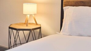 Ein Bett mit weißer Bettwäsche, ein Nachttisch aus Holz mit einer Lampe und ein dunkles Holz-Kopfteil.