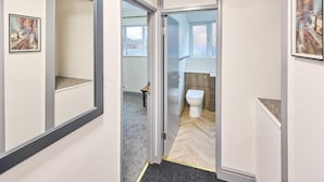 Ein Flur, der zu einem Badezimmer mit Toilette, Dusche und Waschbecken führt.