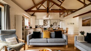 A living room with a sofa, a dining table with a bowl of fruit, and a magazine. - Swallows Nest cottage sleeps 10 guests in 6 bedrooms. (Fakenham)