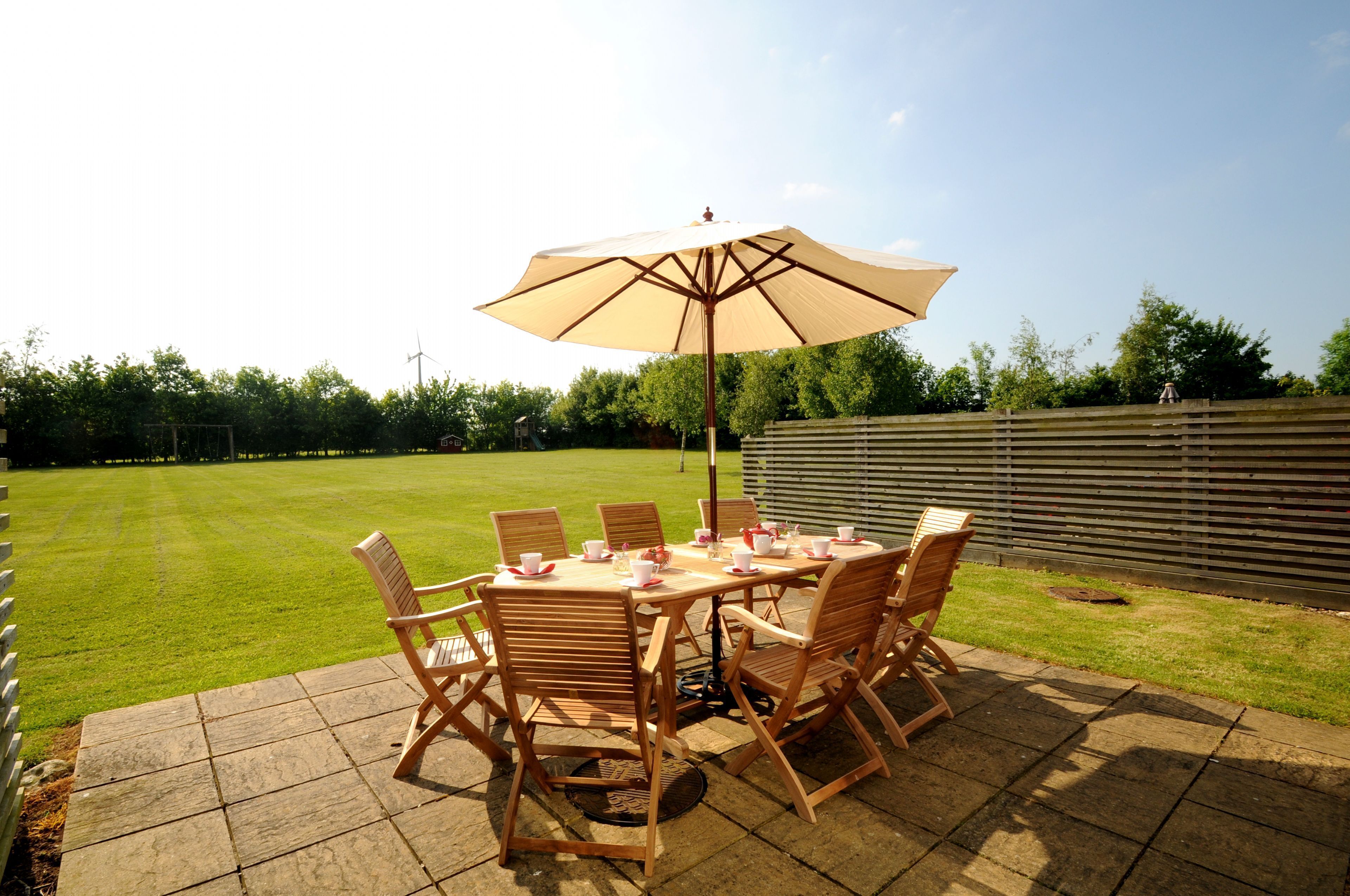 Une terrasse extérieure avec une table et des chaises, un grand parasol et une pelouse verdoyante.