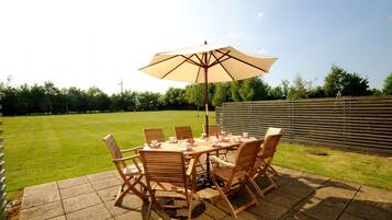 Une terrasse extérieure avec une table et des chaises, un grand parasol et une pelouse verdoyante.