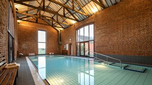 An indoor swimming pool with a tiled floor, wooden benches, and a high ceiling with exposed beams. - Swallows Nest cottage sleeps 10 guests in 6 bedrooms. (Fakenham)