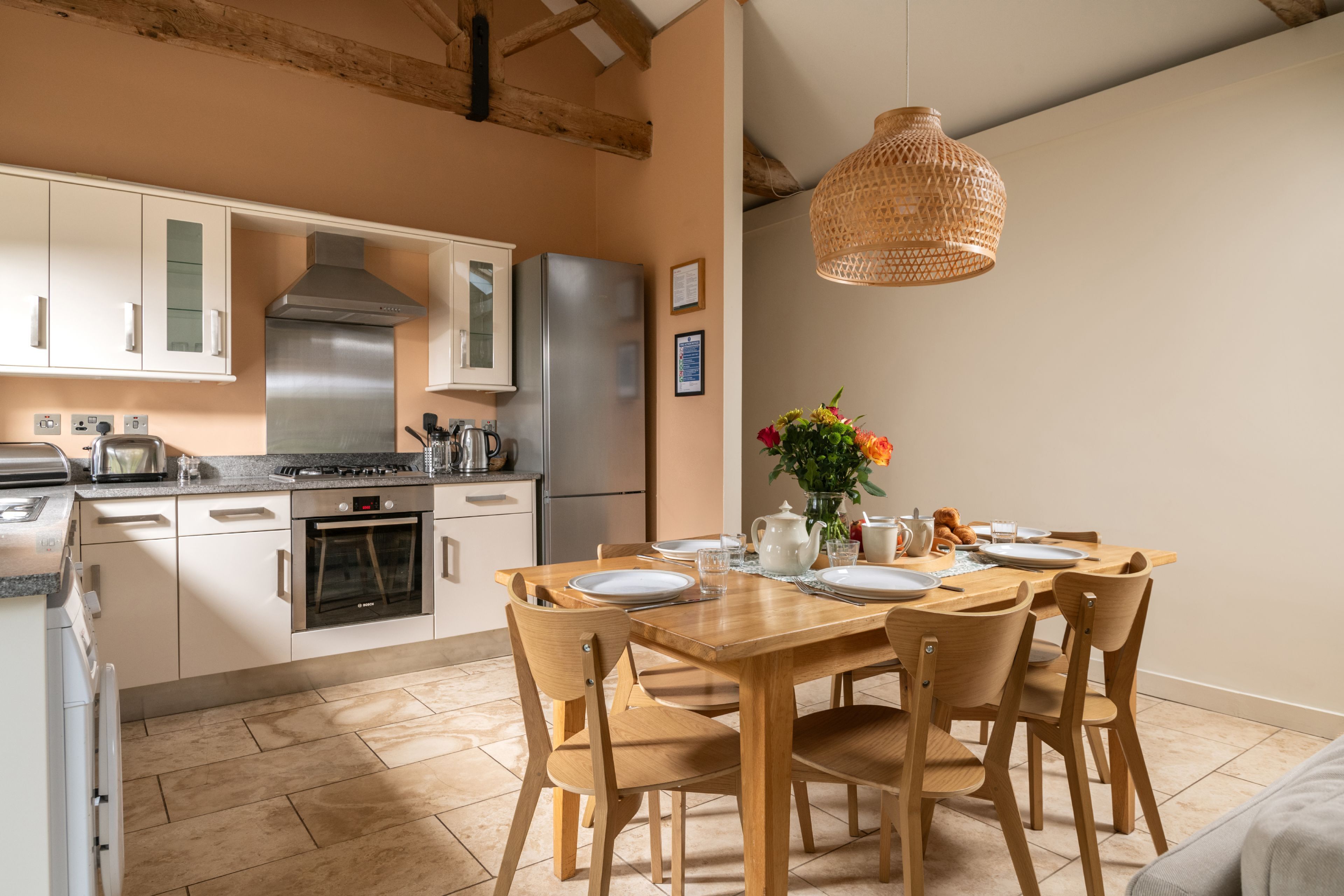 Una cocina moderna con armarios blancos, electrodomésticos de acero inoxidable y una mesa de madera dispuesta para cuatro comensales.