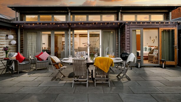 A modern house with a patio area featuring outdoor furniture, a dining table, and a view of the interior.