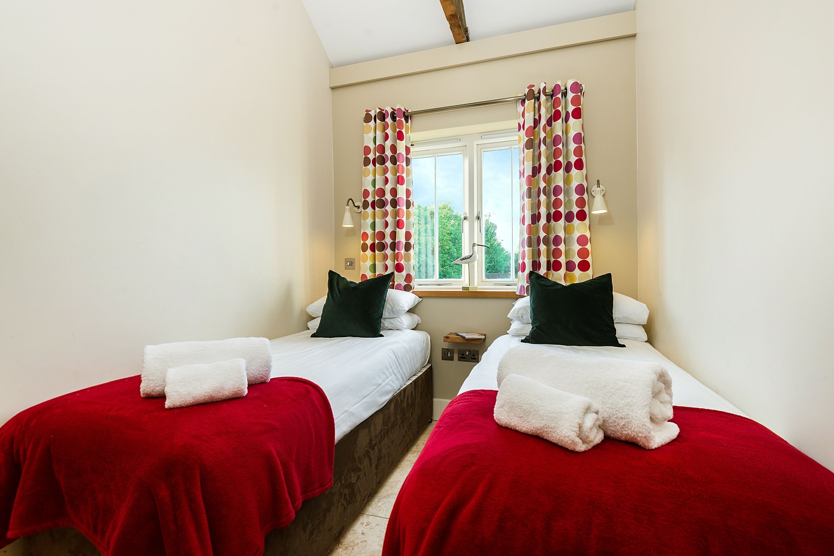 Una habitación de hotel con dos camas, ropa de cama roja y blanca, una ventana con cortinas y una lámpara.