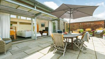 A patio with a table and chairs, a large umbrella, and a view of the interior through glass doors.