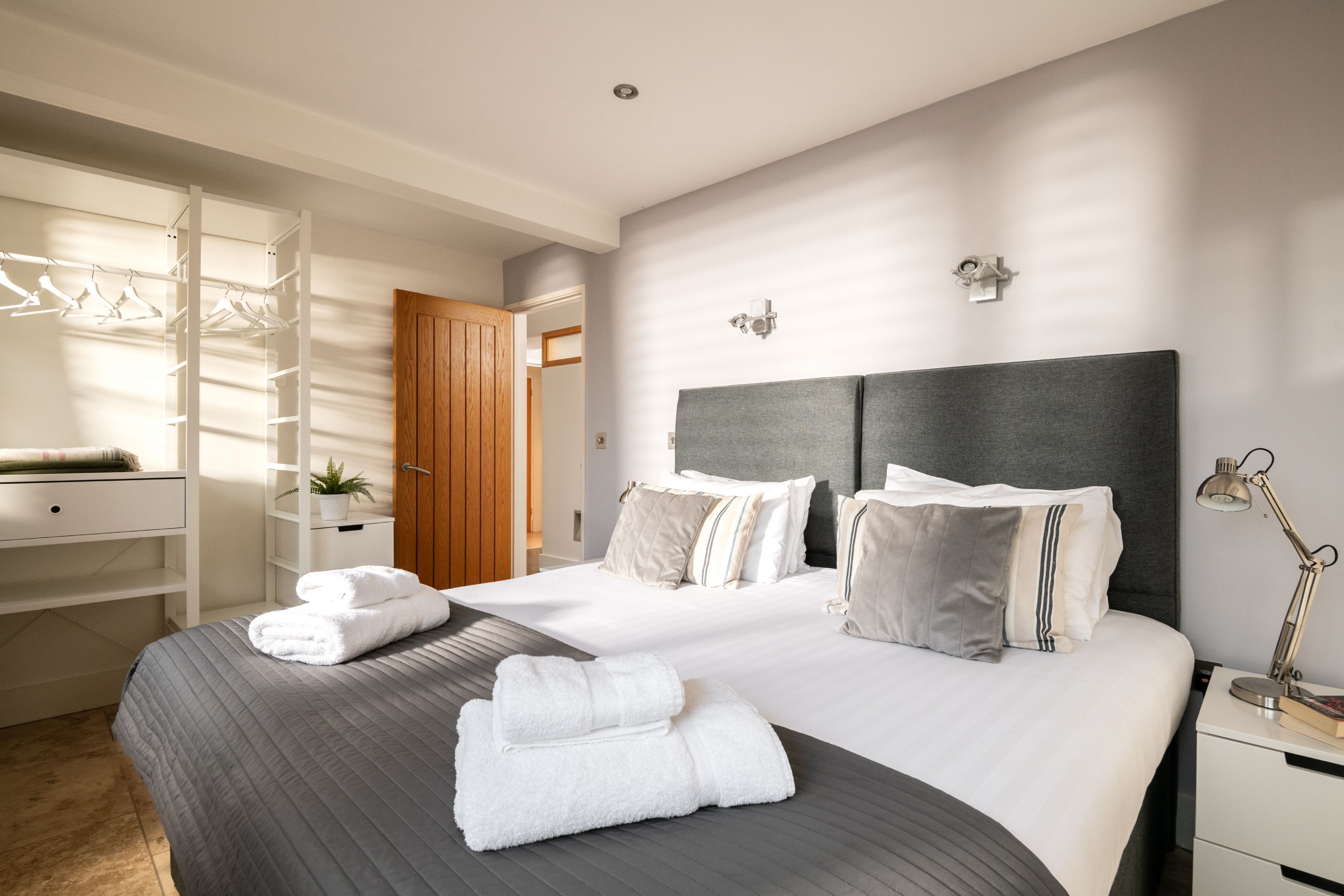A bedroom with a large bed, a wardrobe, a bedside table with a lamp, and a window with blinds.