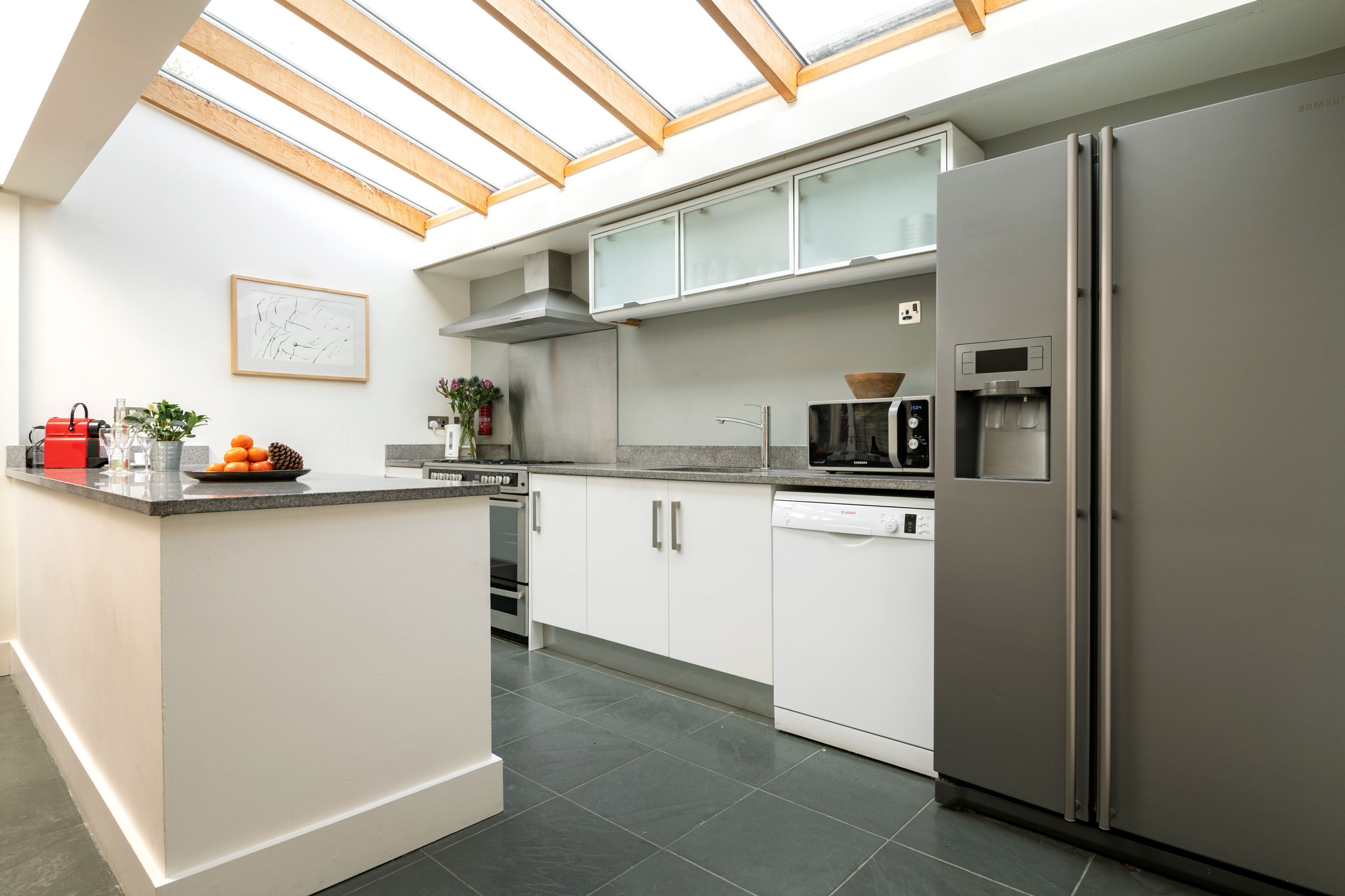 Una cucina moderna con un lucernario, mobili bianchi, forno integrato e frigorifero.