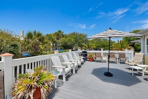 Eine Terrasse mit weißen Adirondack-Stühlen, einem schwarzen Sonnenschirm und Kübelpflanzen.