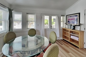 Ein Zimmer mit einem Glastisch, Stühlen, einem Holzregal und einem Fernseher an der Wand.