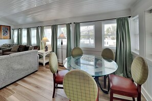 Ein Wohnzimmer mit Glastisch, Stühlen, einer Couch und Vorhängen.