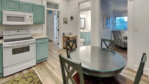 Una cucina con elettrodomestici bianchi, mobili azzurro-verde, un tavolo da pranzo con sedie e vista sull'area soggiorno.