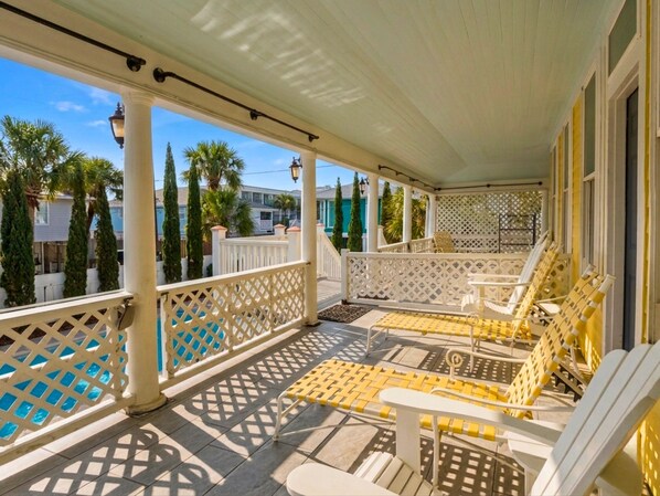 Eine überdachte Veranda mit weißen Geländern, gelb-weißer Gartenmöbel und Blick auf die umliegende Nachbarschaft.