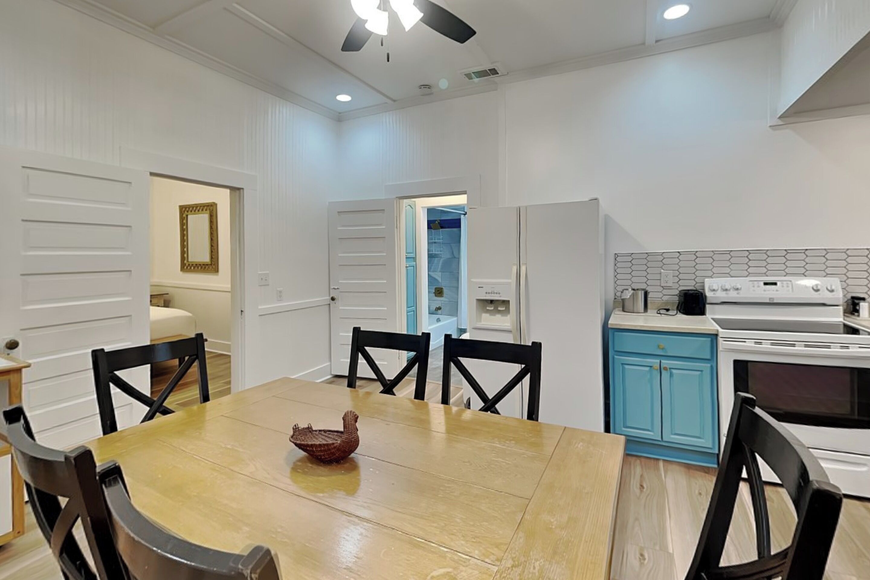 A dining area with a wooden table and chairs, a kitchen with white appliances, and a blue cabinet.