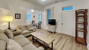 Un salon comprenant un canapé, une table basse, un téléviseur, un ventilateur de plafond et une bibliothèque en bois.
