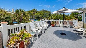 Eine Terrasse mit weißen Adirondack-Stühlen, einem schwarzen Sonnenschirm und Kübelpflanzen.