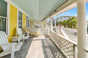 A covered porch with white Adirondack chairs, a small table, and a bench. - The Georgianne Manor | Historic Inn, Private Pool, Near Beach (Tybee Island)
