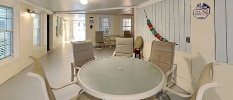A dining area with a round glass table and white chairs, a no-smoking sign, and a view of the adjacent room.
