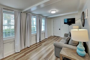 Ein Wohnzimmer mit Sofa, Lampe, Fernseher und einem Fenster mit Vorhängen.
