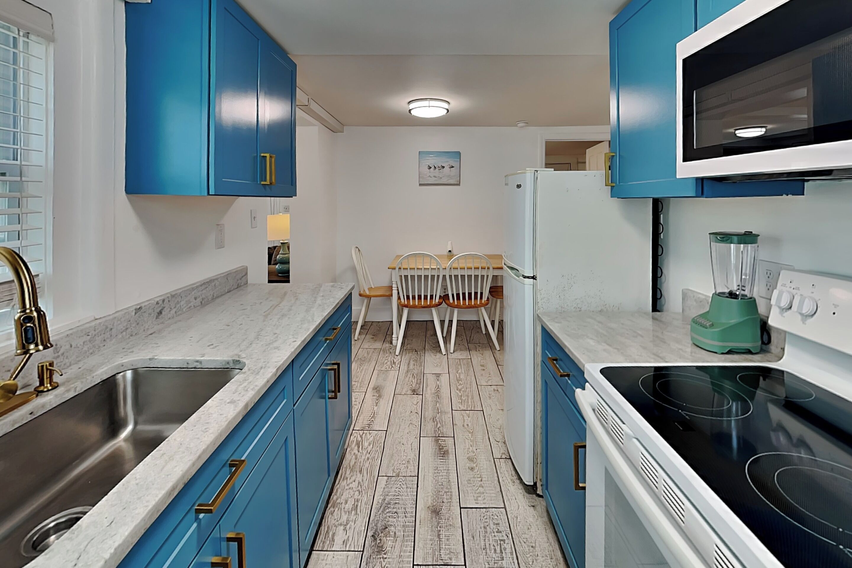 A kitchen with blue cabinets, a stainless steel sink, a white refrigerator, a microwave, and a blender.