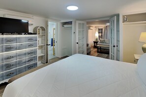 Ein Hotelzimmer mit einem großen Bett, einem Fernseher, einem Kleiderschrank mit mehreren Schubladen und einer Tür zu einem Sitzbereich mit einer Lampe.