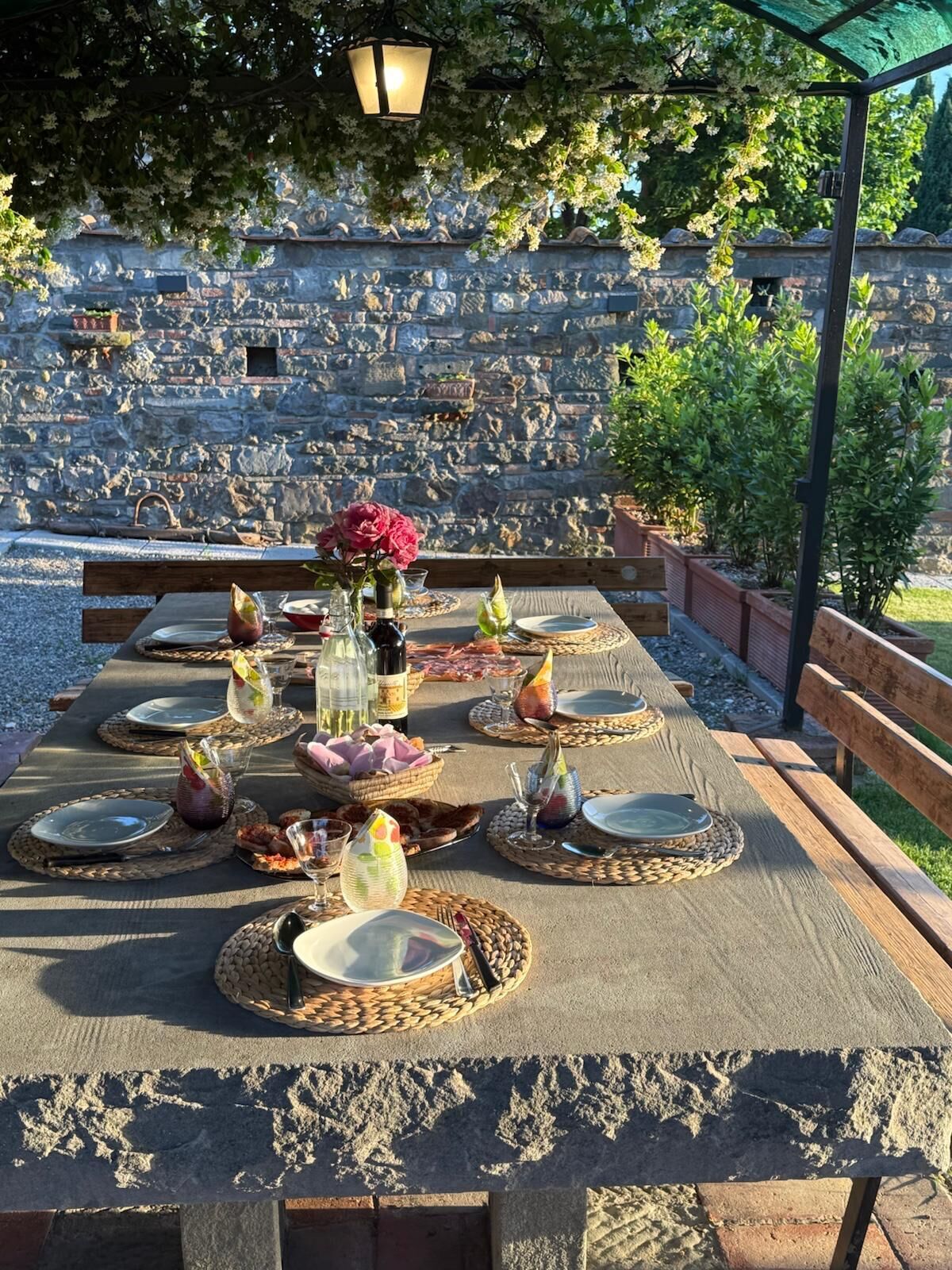 An outdoor dining area with stone walls, a pergola, and a view of a stone amphitheater.
