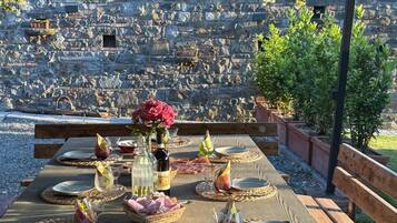 An outdoor dining area with stone walls, a pergola, and a view of a stone amphitheater.