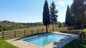A rectangular swimming pool with a stone border, surrounded by a wooden fence and stone steps, set against a backdrop of rolling hills and trees. - An authentic corner of Tuscany. Relaxation, good food, close to Florence, Siena, Pisa (Toscana)