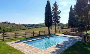 A rectangular swimming pool with a stone border, surrounded by a wooden fence and stone steps, set against a backdrop of rolling hills and trees. - An authentic corner of Tuscany. Relaxation, good food, close to Florence, Siena, Pisa (Toscana)