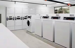 A laundry facility with multiple washing machines and dryers, a clean floor, and a window providing natural light. - Resort Stay 10 Min to Disney World + Pool (Kissimmee)