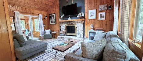 Ein Holzblock-Interieur mit Kamin, Sofas, einem Fernseher und einem großen Fenster.