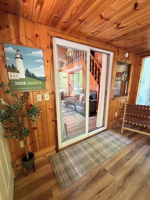 Innenansicht einer Holzhütte mit Glastür zu einem Wohnbereich, einem Schild mit der Aufschrift 'Door County Wisconsin' und einer hölzernen Bank.