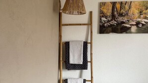Ein Zimmer mit einem Etagenbett, einer Holzleiter, Handtüchern, einer gewebten Leuchte und einem Gemälde eines Waldflusses.