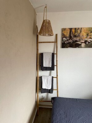 Ein Zimmer mit einem Etagenbett, einer Holzleiter, Handtüchern, einer gewebten Leuchte und einem Gemälde eines Waldflusses.