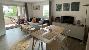 Ein modernes Wohnzimmer mit einer Couch, einem Esstisch, Stühlen, einem Fernseher und Kunstwerken an der Wand.