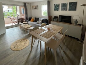 Ein modernes Wohnzimmer mit einer Couch, einem Esstisch, Stühlen, einem Fernseher und Kunstwerken an der Wand.