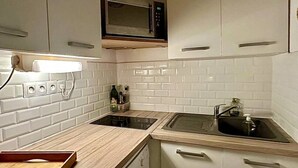 Eine kleine Küche mit weißen Fliesenwänden, einer Mikrowelle, zwei Spülen und einer Holz Arbeitsplatte.