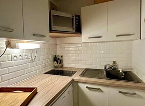 Eine kleine Küche mit weißen Fliesenwänden, einer Mikrowelle, zwei Spülen und einer Holz Arbeitsplatte.