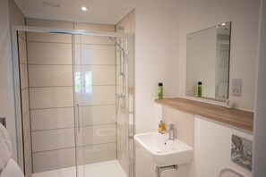 A modern bathroom with a glass shower enclosure, a white sink, and a mirror above it. - Stylish 2 bed home near Trafford  (Eccles)
