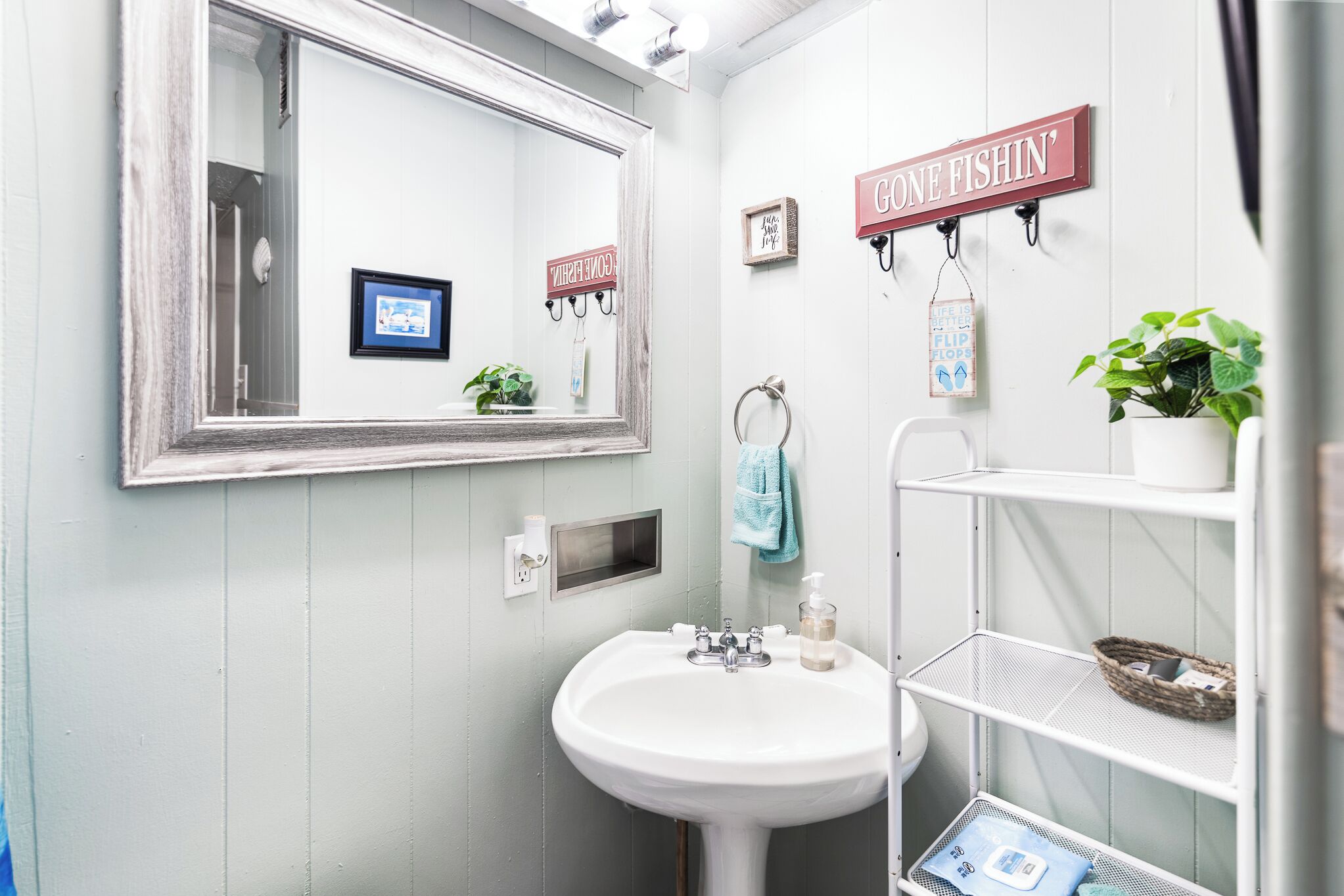 Kylpyhuone, jossa on valkoinen pesuallas, peili ja hylly, jossa on hygieniatuotteita.