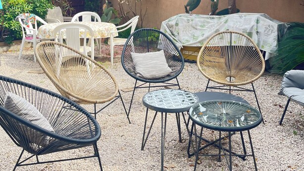 Un espace extérieur aménagé avec des chaises en osier, une table ronde et une table couverte.