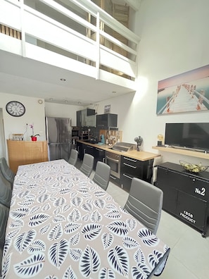 A modern kitchen with a dining area, a loft bedroom, and a living room with a TV. - Le clos des mimosas (Bormes-les-Mimosas)