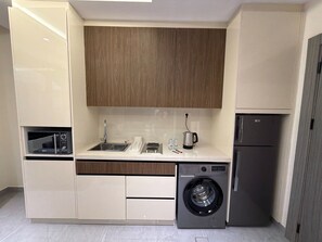 A compact kitchen with a built-in washing machine, a microwave, and a refrigerator. - 101 JRE Apartment With Stunning Boulevar (Amman)