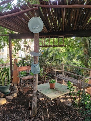 Un espace extérieur rustique aménagé avec un banc en bois, une table en métal et une mangeoire à oiseaux suspendue.
